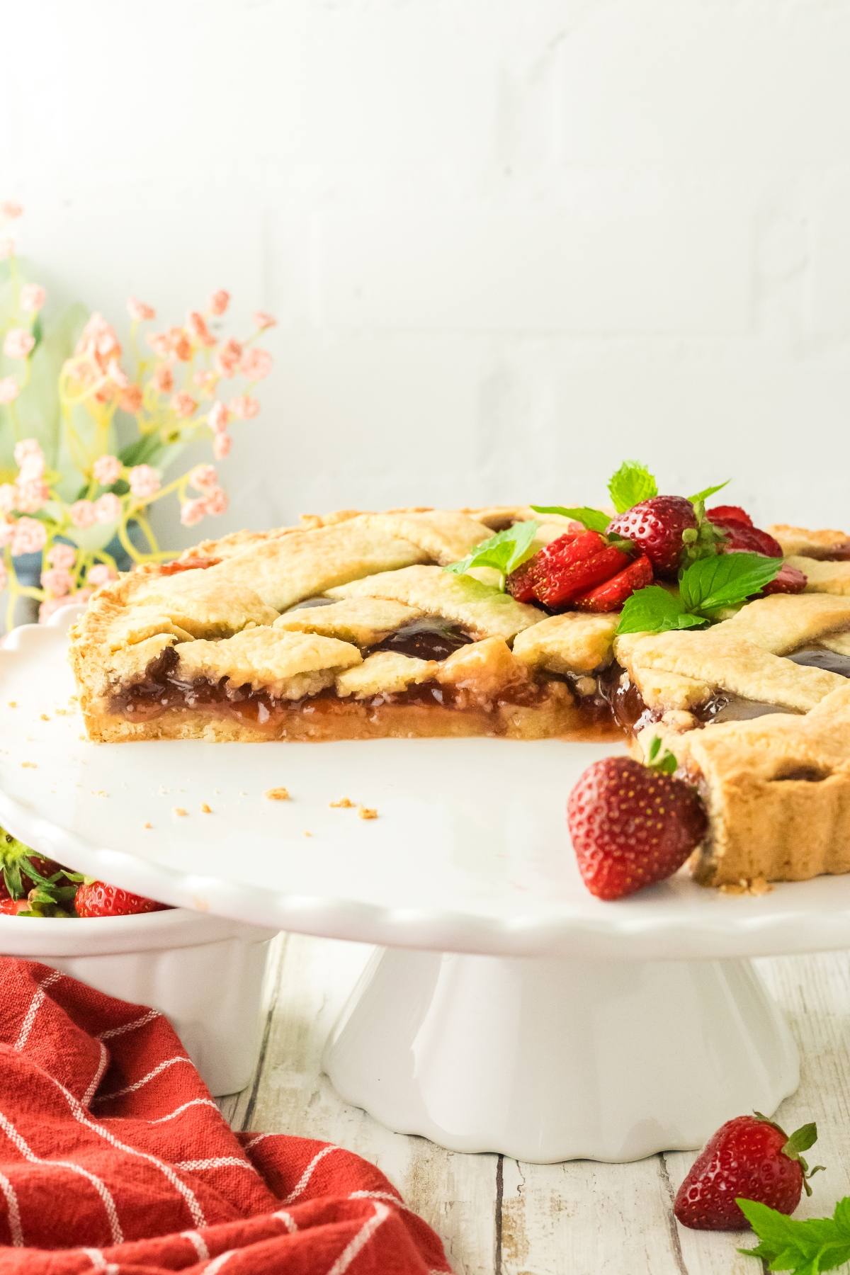 A half-eaten strawberry pie on a white cake stand, garnished with fresh strawberries and mint leaves.