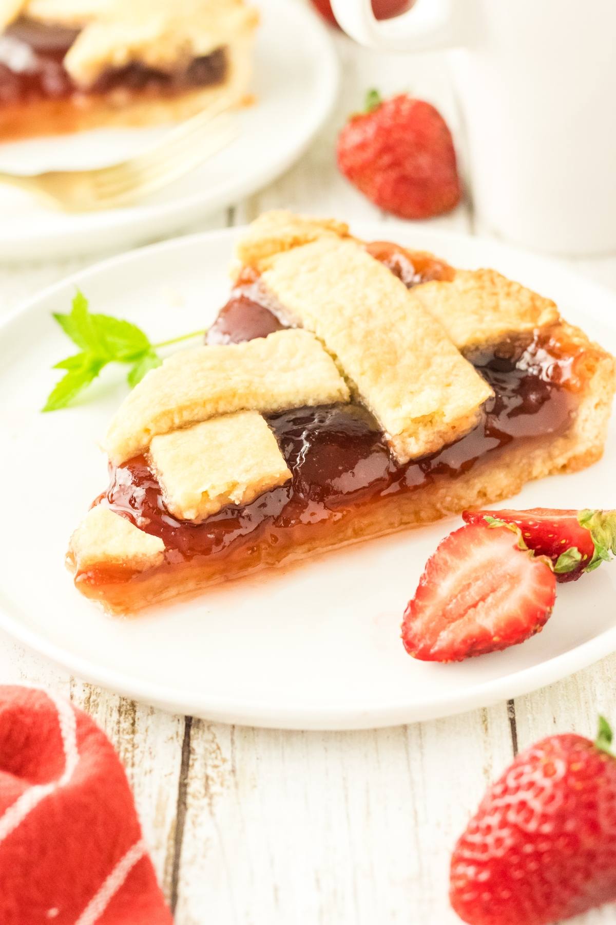 A slice of strawberry pie with lattice crust on a white plate, garnished with fresh strawberries.