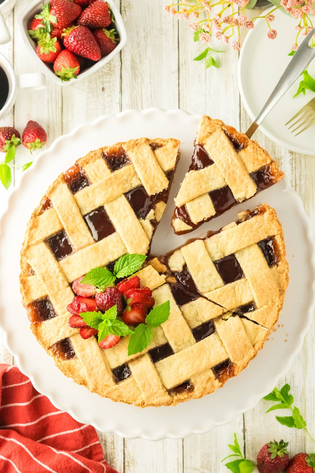 A lattice-top strawberry pie garnished with mint and sliced strawberries on a white plate.