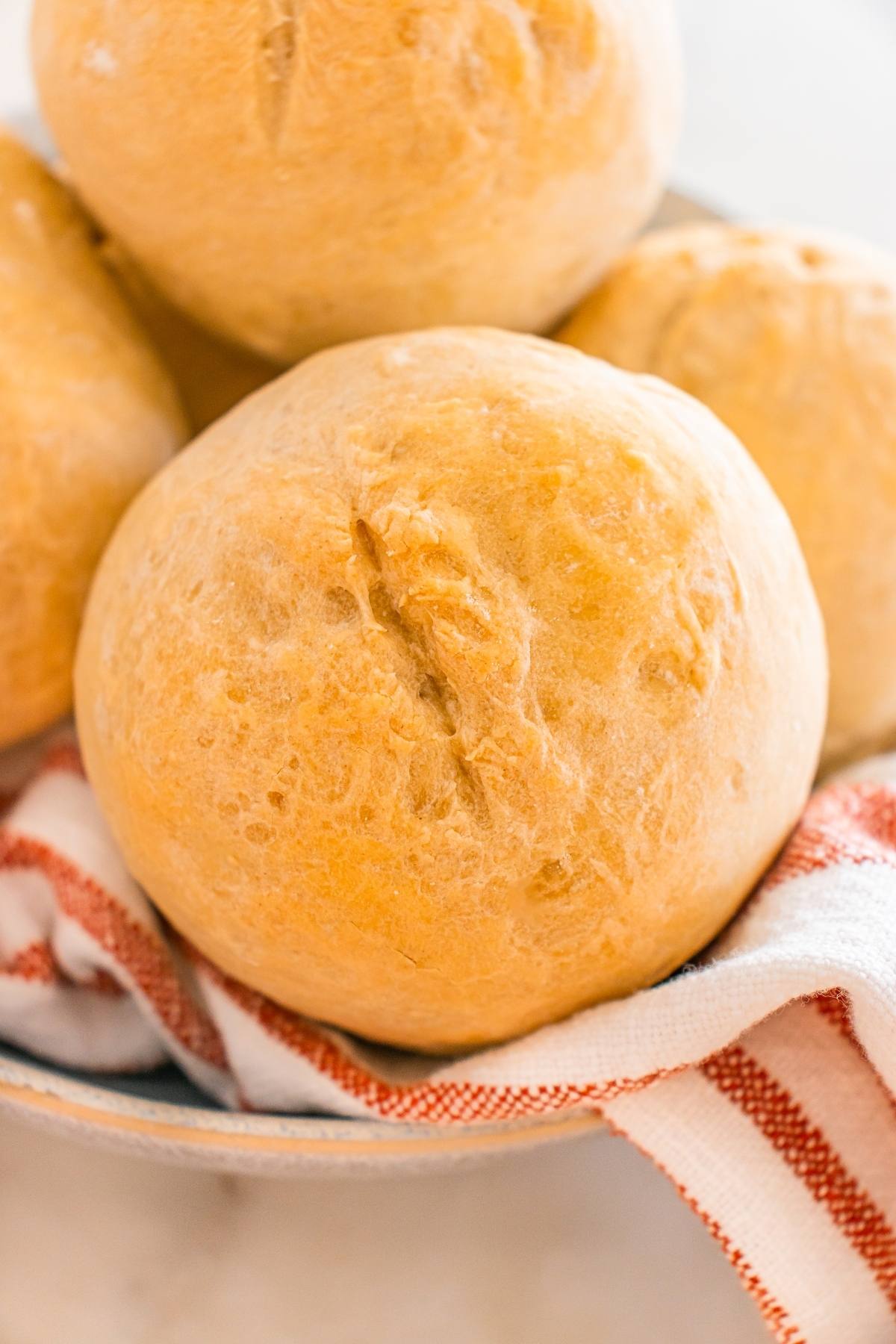 A close-up of golden brown bread rolls in a bowl with a red and white striped cloth.