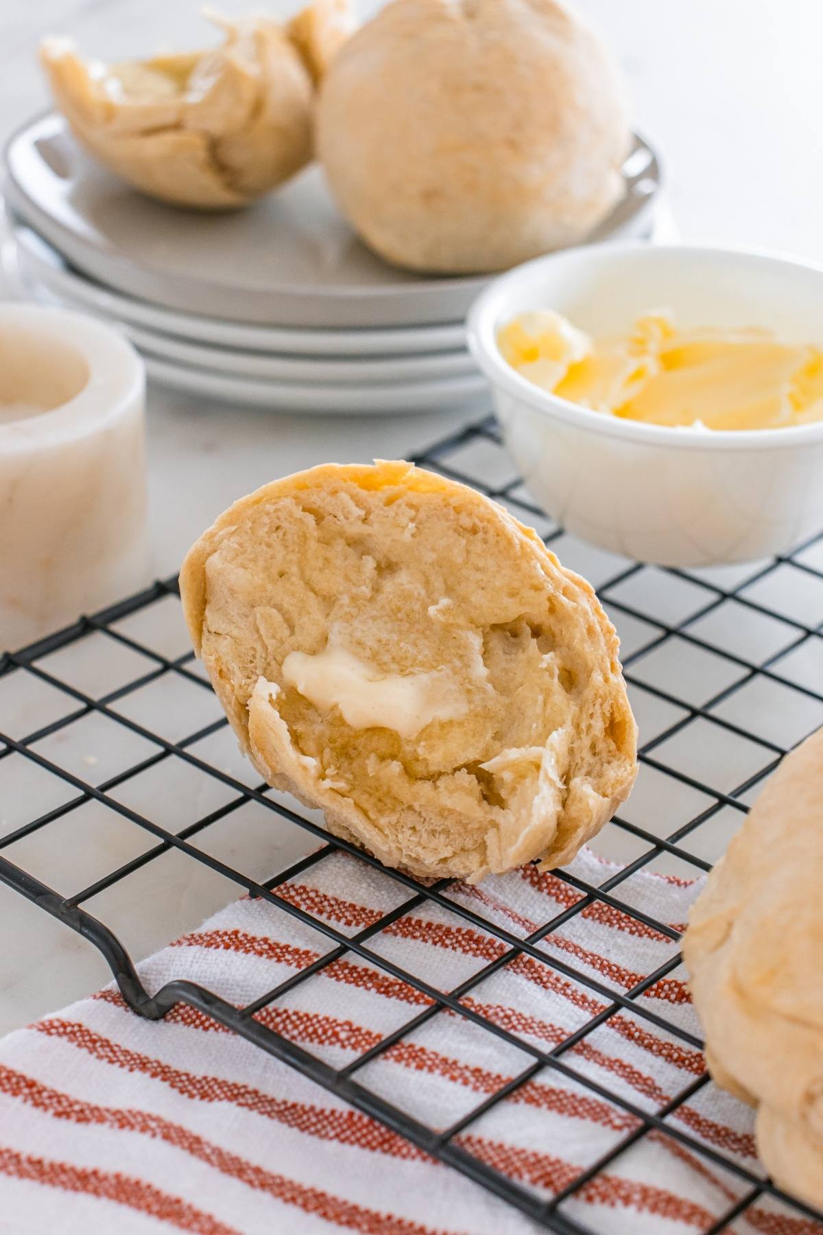 A biscuit split open with melting butter on a cooling rack, with more biscuits and butter in the background.
