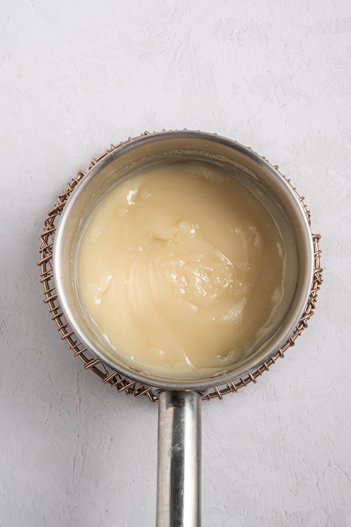 A saucepan filled with a thick, creamy white mixture on a light textured surface.
