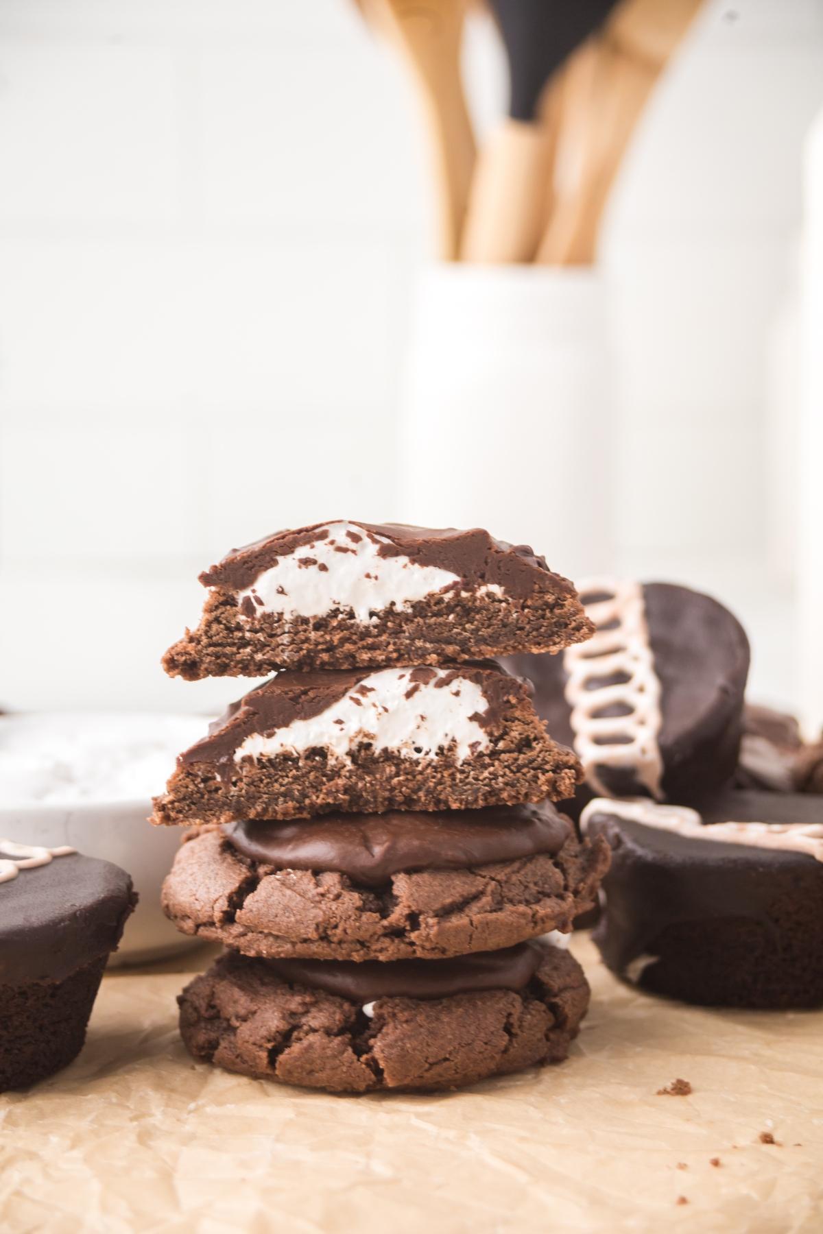 Stacked chocolate cookies with marshmallow filling, one split in half, on a parchment surface.