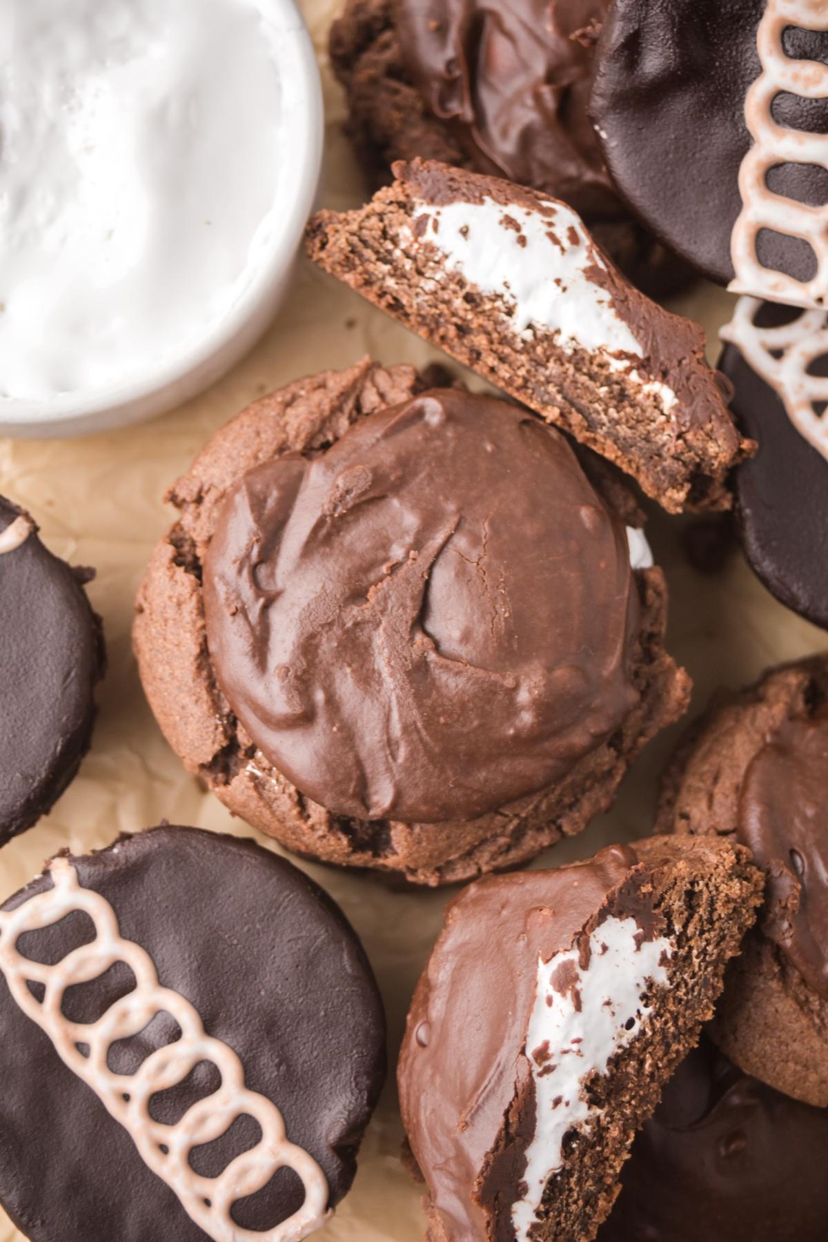 Chocolate sandwich cookies with cream filling, some whole and some halved, next to a bowl of white cream.