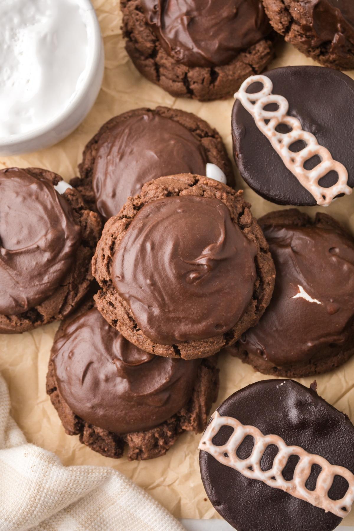 Chocolate cookies with glossy frosting, some topped with white icing swirls, on parchment paper.