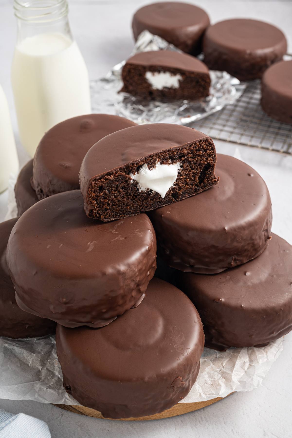 A stack of chocolate-coated cakes with cream filling, with a bottle of milk in the background.