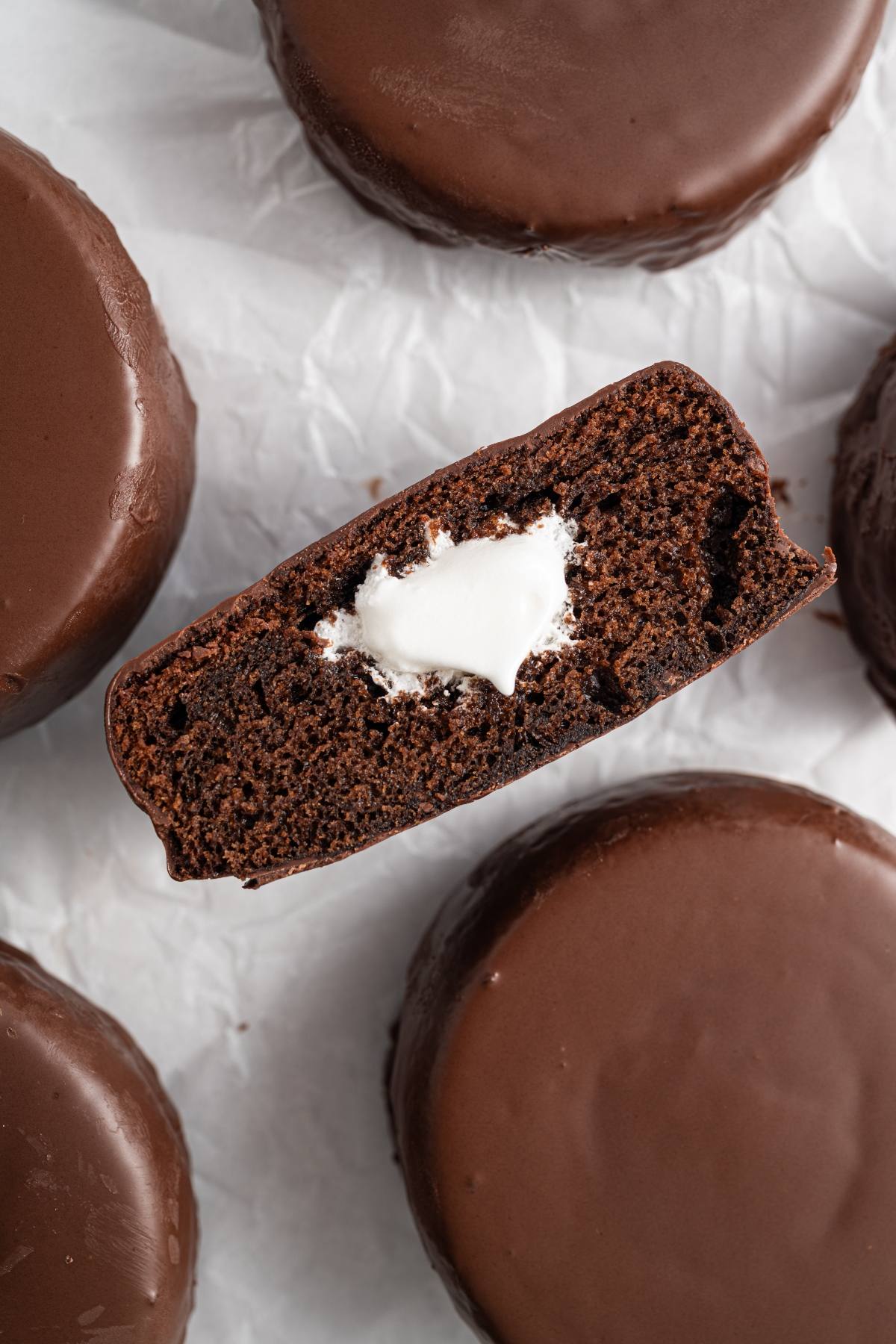 A chocolate cake snack with a creamy white filling inside, surrounded by other chocolate-covered cakes.