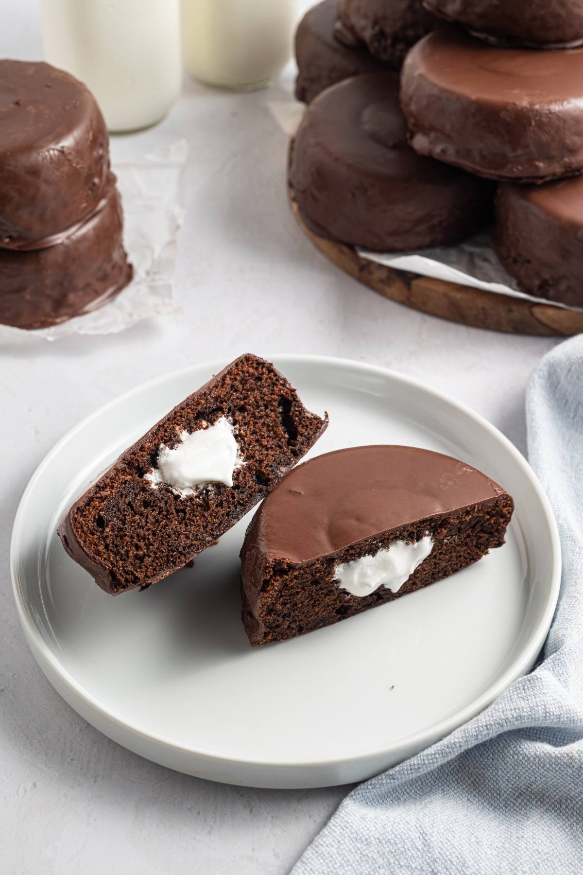 Chocolate snack cake with creamy filling cut in half on a white plate, with more cakes in the background.