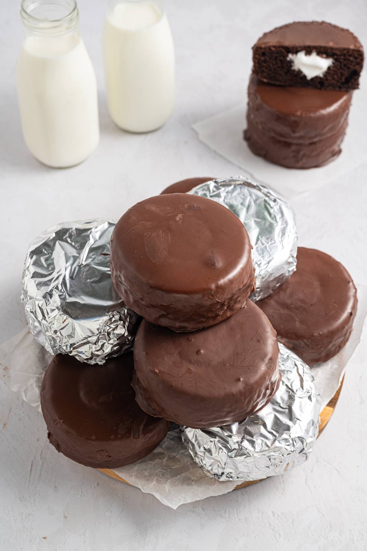 A plate of chocolate-covered snack cakes, some wrapped in foil, with two bottles of milk in the background.