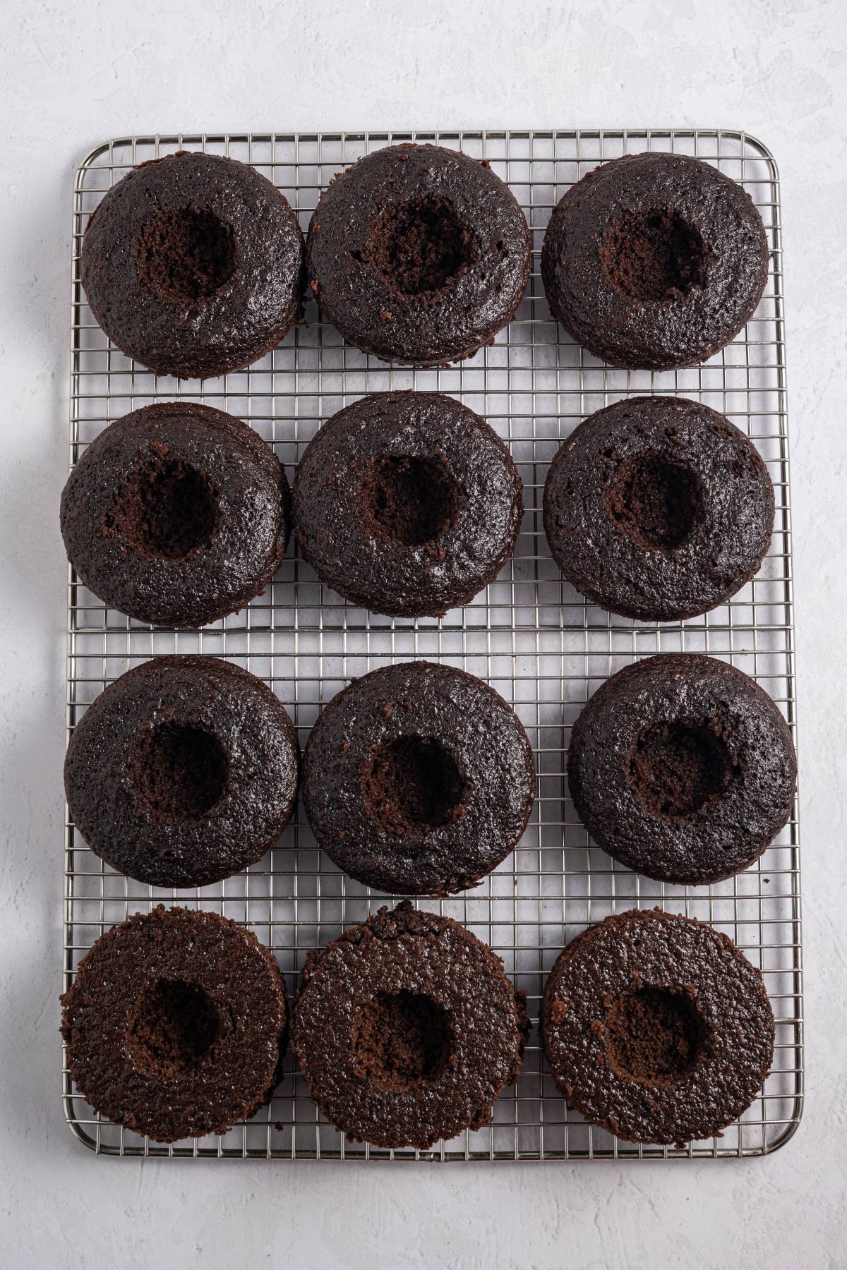 Twelve chocolate donuts cooling on a wire rack, arranged in three rows of four on a white background.