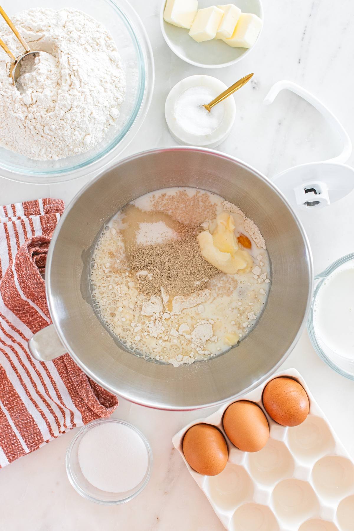 Baking ingredients—flour, eggs, sugar, butter, and yeast—arranged on a counter with a mixing bowl.