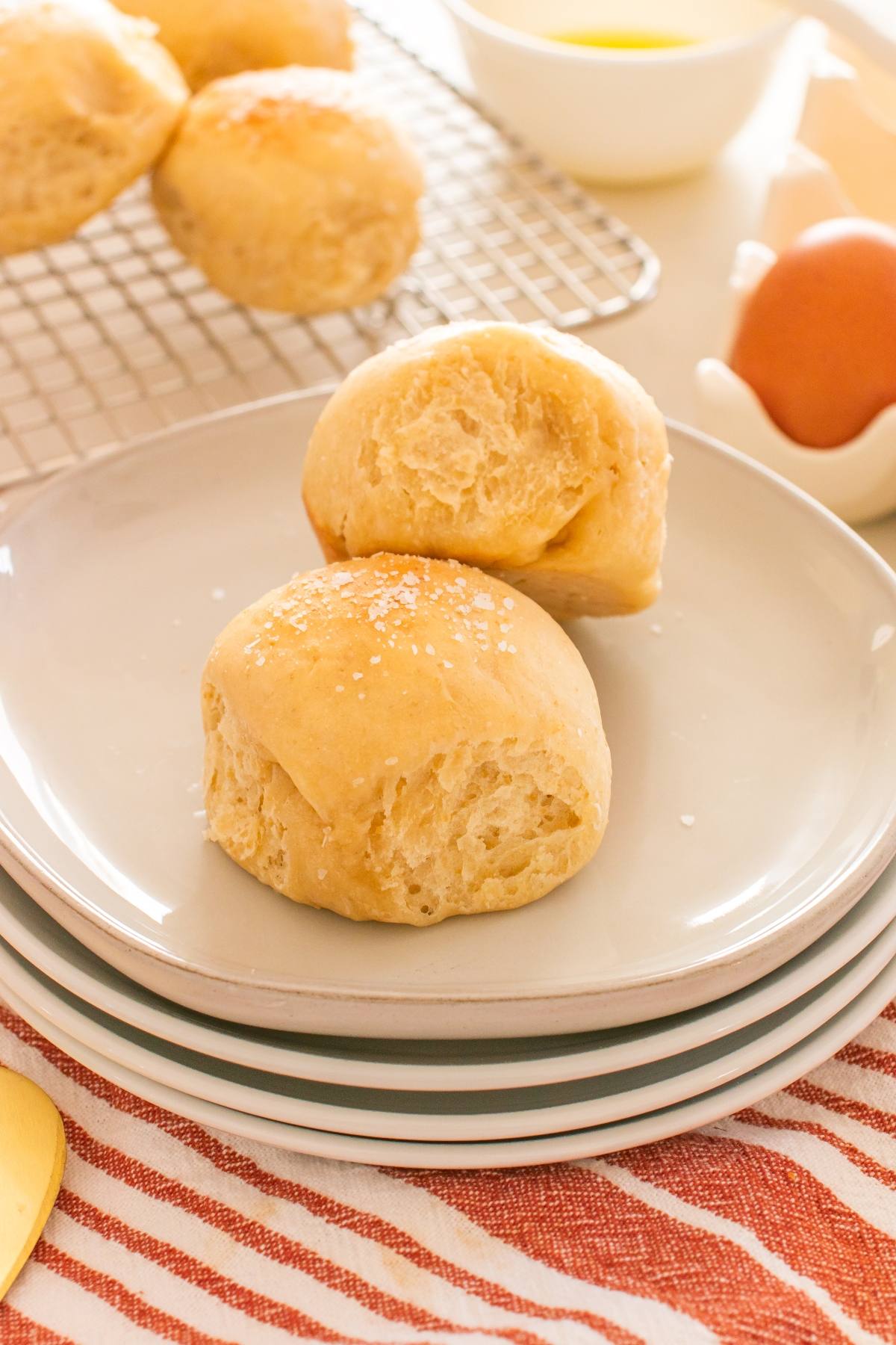 Two golden dinner rolls with flaky texture and sea salt on top, served on a stacked plate.