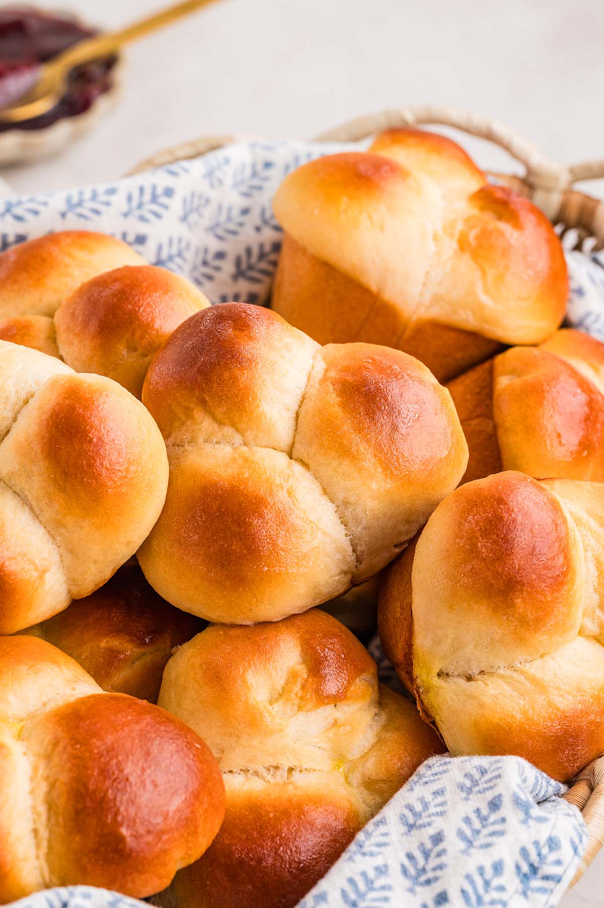 Golden brown cloverleaf rolls rest in a basket lined with a white and blue patterned cloth.