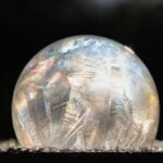 A frozen soap bubble with icy patterns glistens in the sunlight, surrounded by small ice crystals—a magical result when you learn how to make frozen bubbles on a chilly winter day.