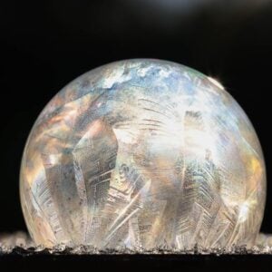 A frozen soap bubble with icy patterns glistens in the sunlight, surrounded by small ice crystals—a magical result when you learn how to make frozen bubbles on a chilly winter day.