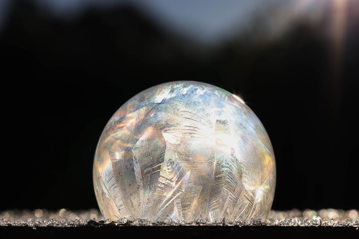 A frozen soap bubble with icy patterns glistens in sunlight against a dark, blurred background, offering inspiration for anyone curious about how to make frozen bubbles.