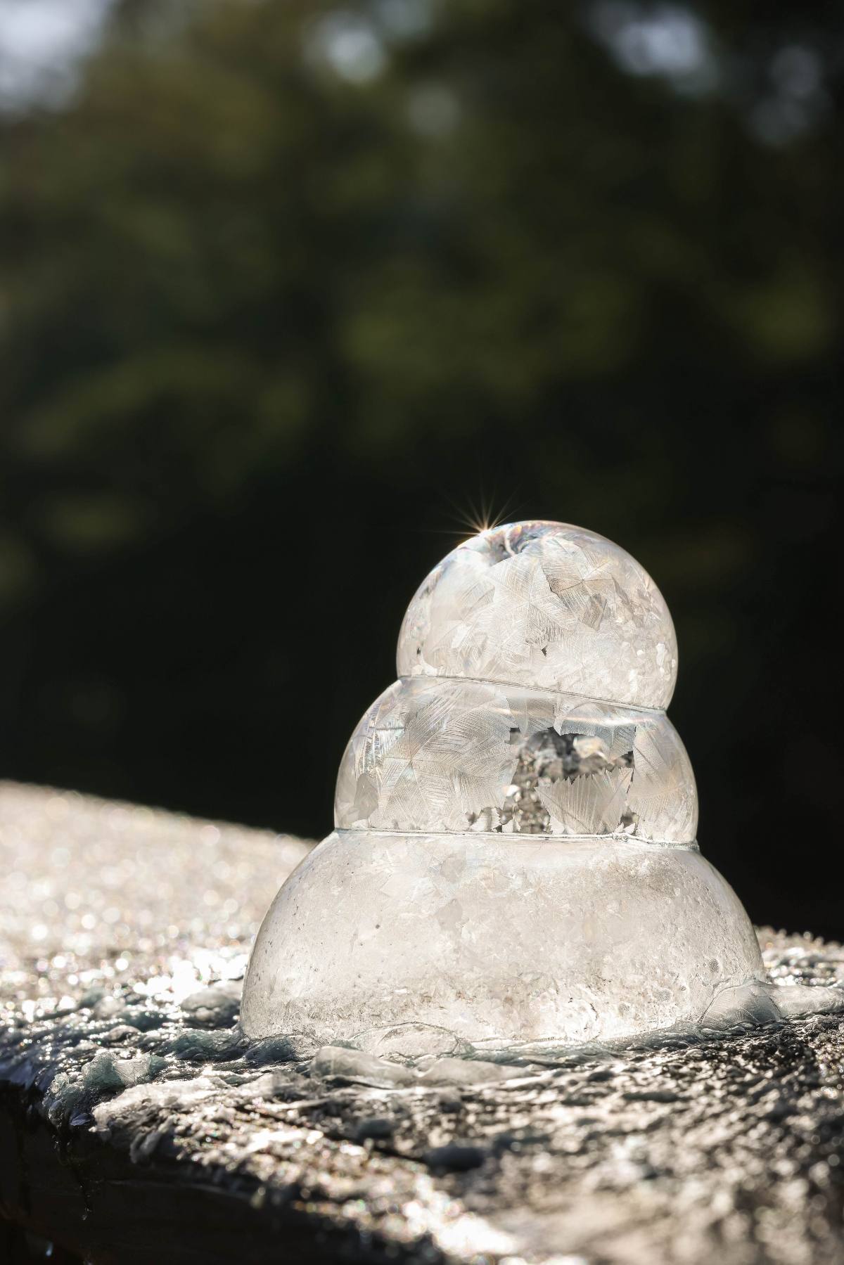 Three stacked clear ice spheres glistening in sunlight on a frosty wooden surface outdoors.
