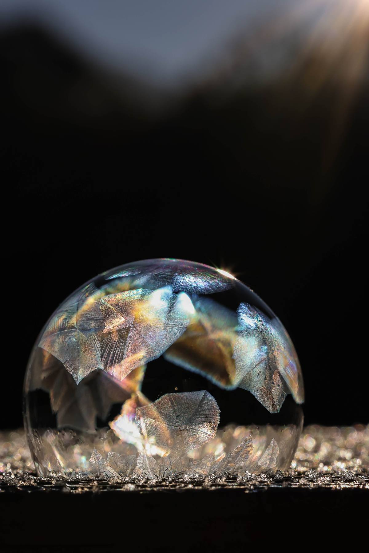 A frozen soap bubble with delicate ice crystals reflects light against a dark, blurred background.