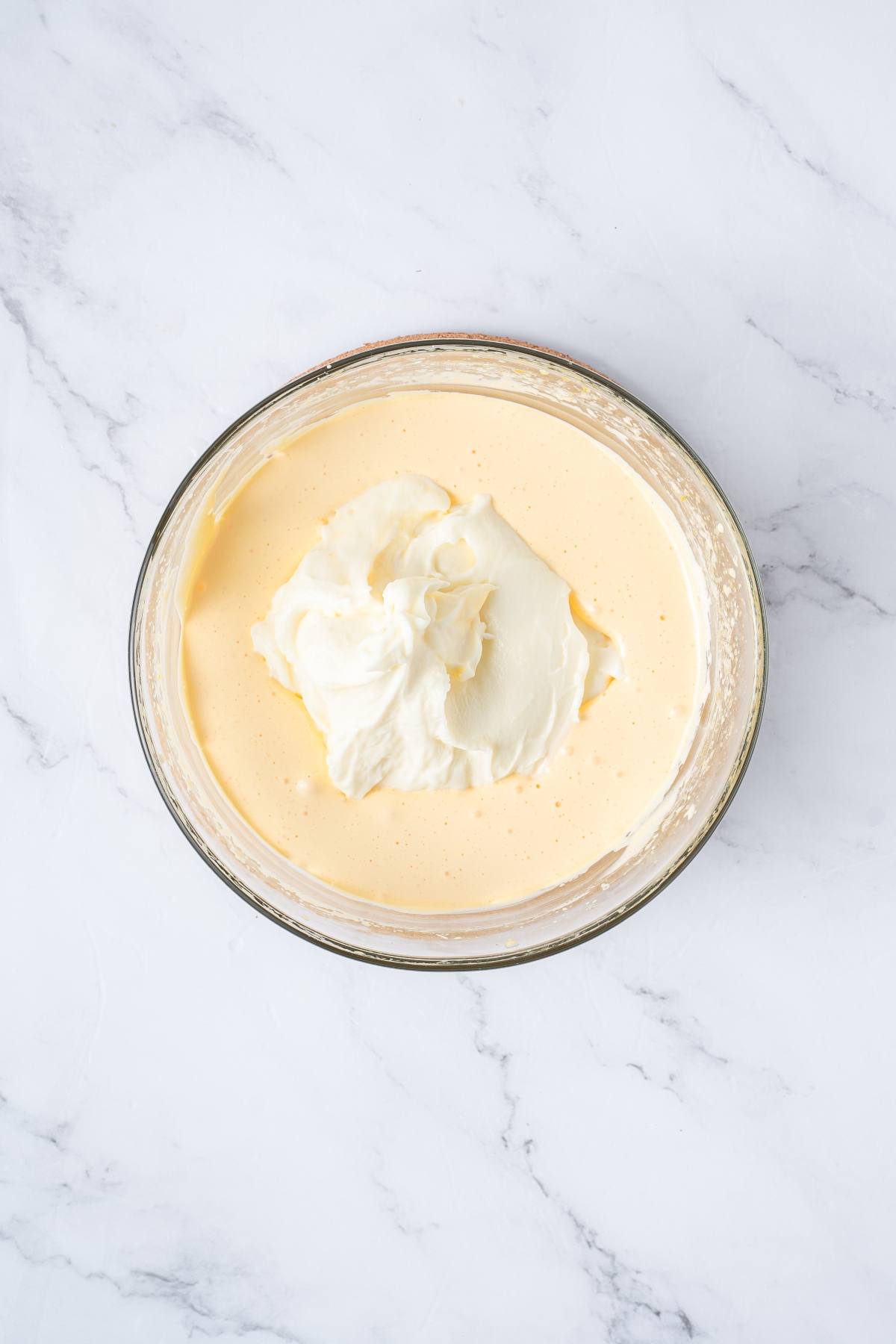 A glass bowl with creamy mixture and a dollop of whipped cream on a marble surface.