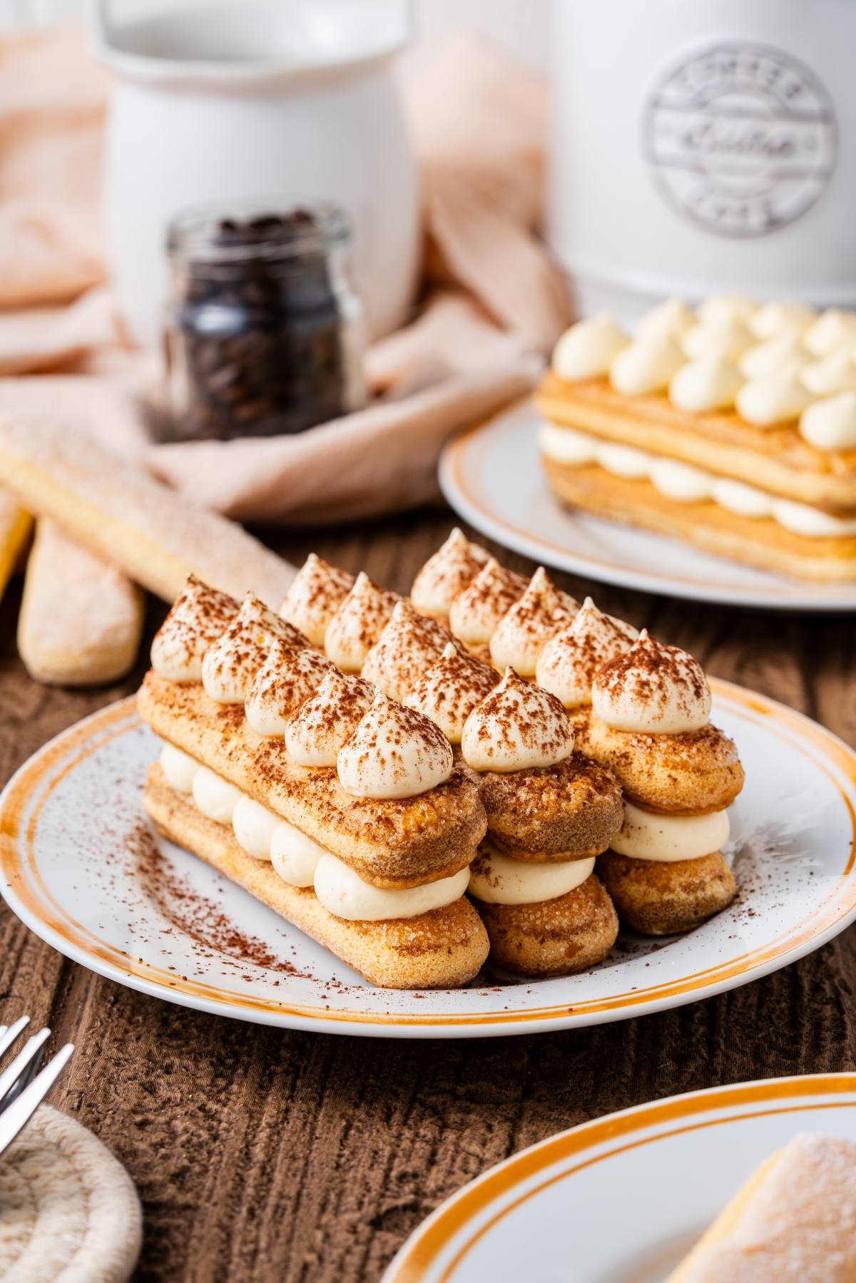 Tiramisu desserts with cream and cocoa powder on plates, set on a rustic wooden table.