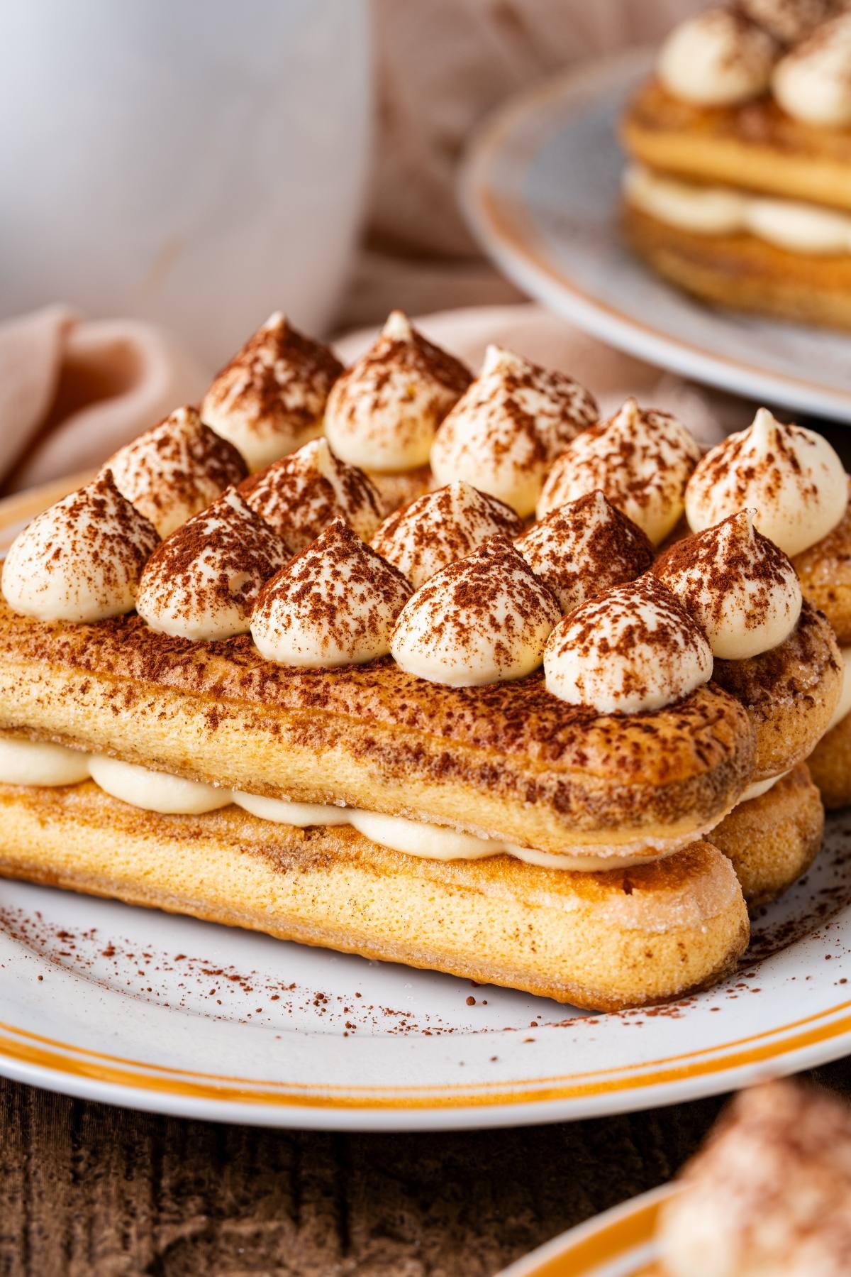 A close-up of a tiramisu dessert with cream dollops and cocoa powder on a white plate.