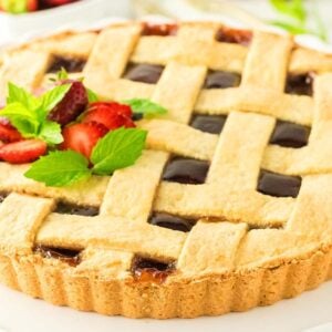 Lattice-topped crostata di marmellata garnished with fresh strawberries and mint leaves on a white plate.