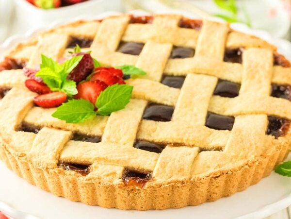 Lattice-topped crostata di marmellata garnished with fresh strawberries and mint leaves on a white plate.