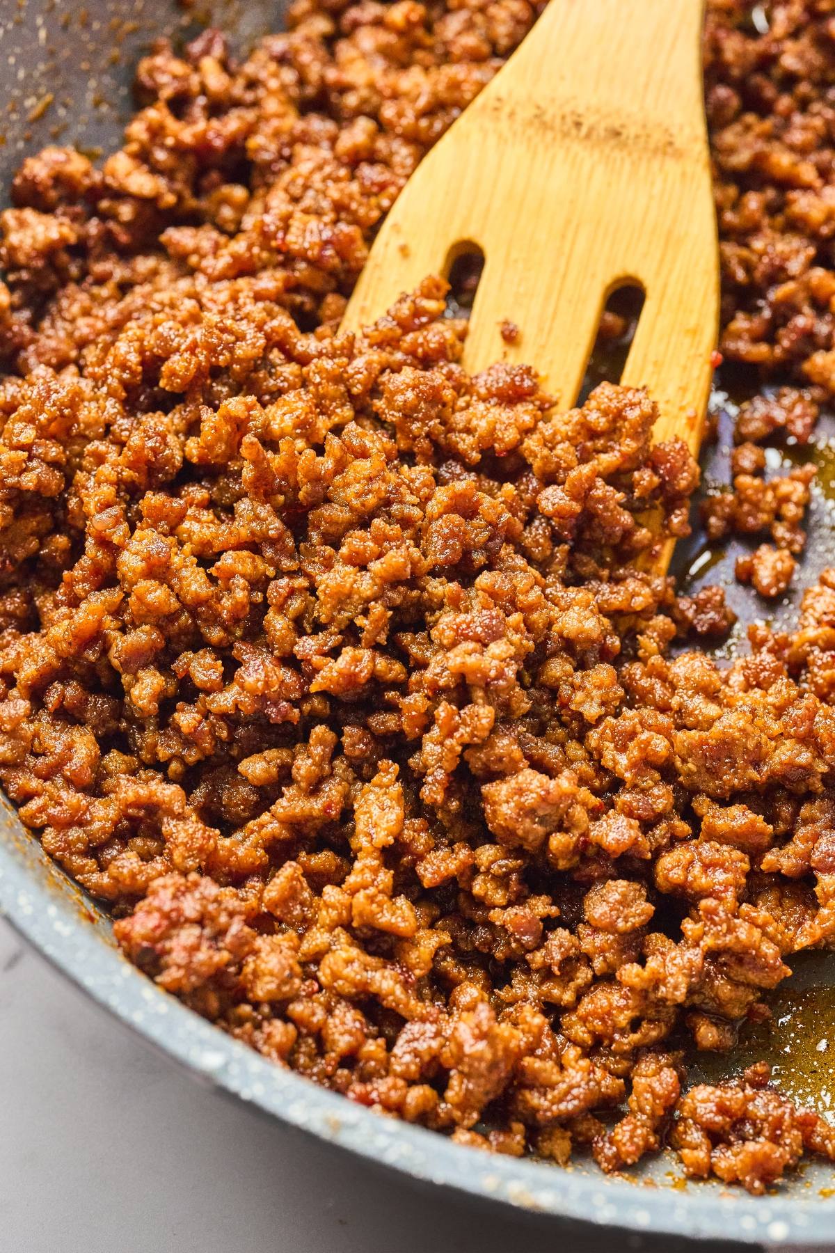 Cooked ground meat with spices being stirred in a pan with a wooden spatula.