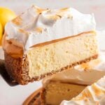 A slice of Lemon Meringue Cheesecake with caramel and fluffy meringue topping is being served from the whole cake.