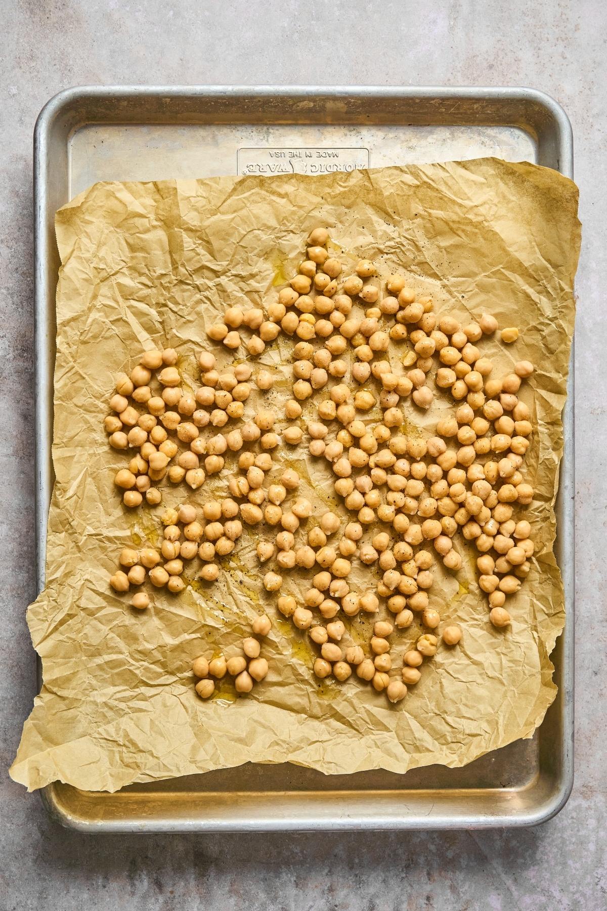 Chickpeas spread on parchment-lined baking sheet, ready to be roasted.