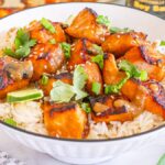Miso salmon bites on white rice, garnished with green onions, cilantro, and sesame seeds in a bowl.