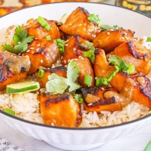 Miso salmon bites on white rice, garnished with green onions, cilantro, and sesame seeds in a bowl.