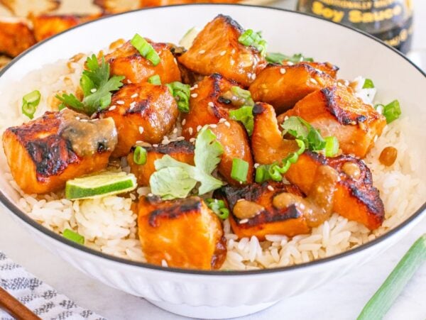 Miso salmon bites on white rice, garnished with green onions, cilantro, and sesame seeds in a bowl.