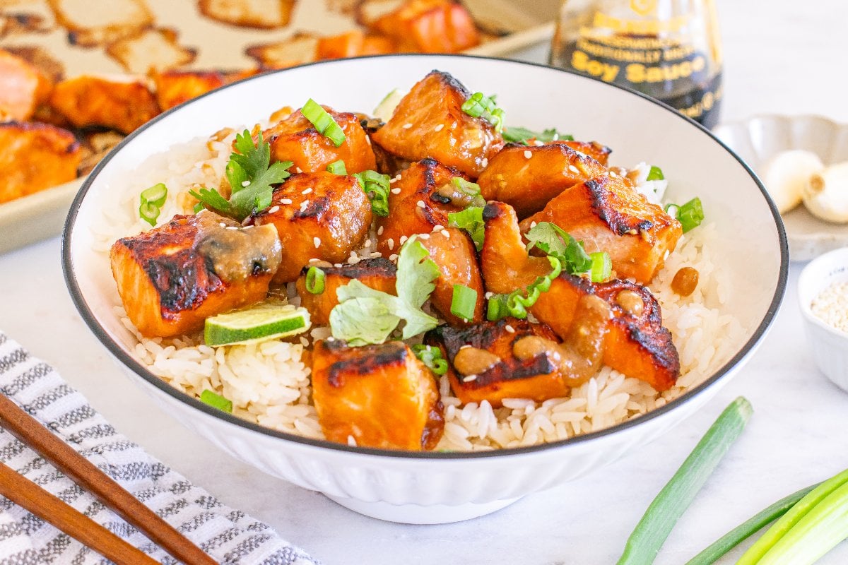 A bowl of rice topped with miso salmon bites, green onions, cilantro, and a lime wedge.