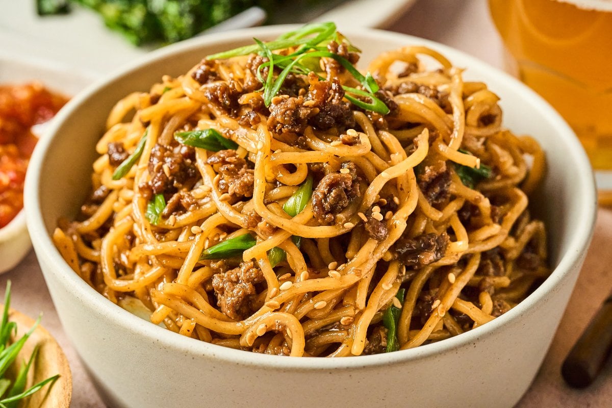 A bowl of Mongolian Ground Beef Noodles mixed with ground meat, green onions, and sesame seeds, garnished with sliced scallions.