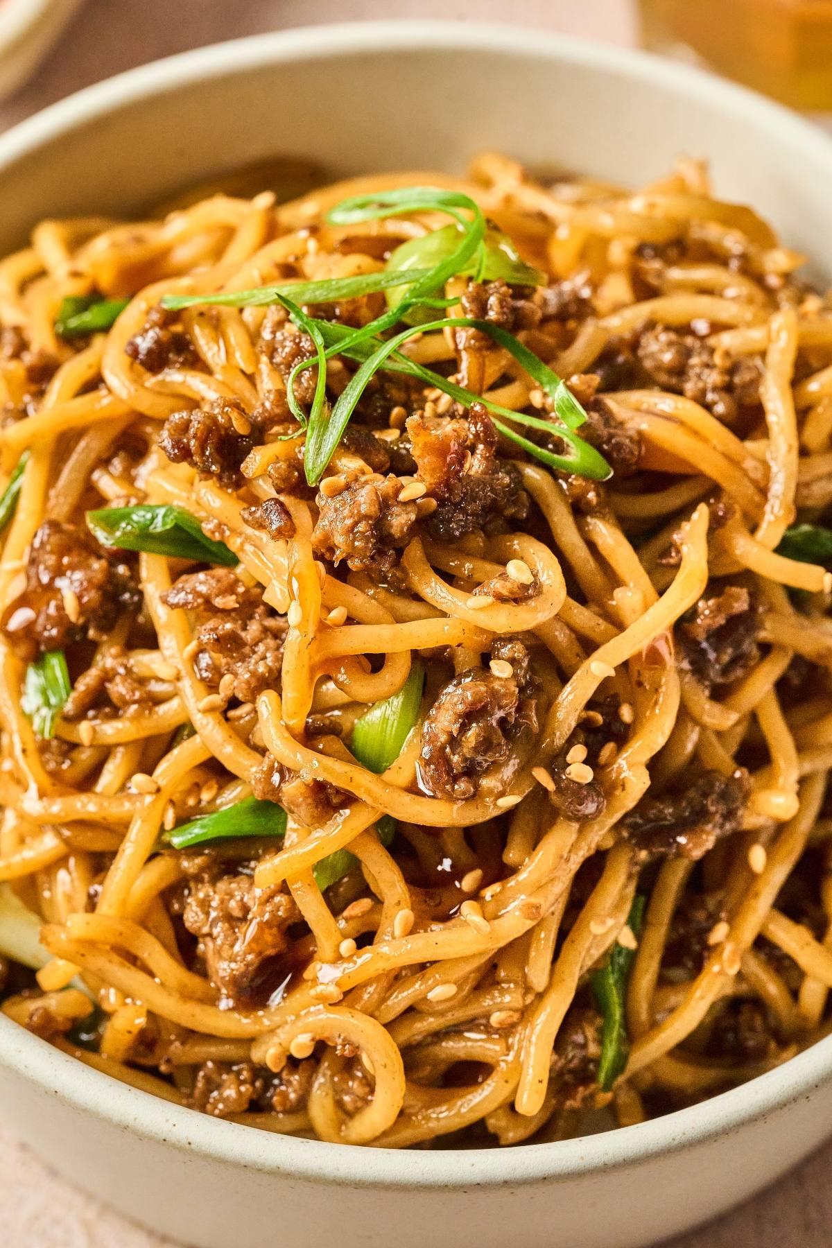 Bowl of stir-fried noodles with ground meat, green onions, and sesame seeds.