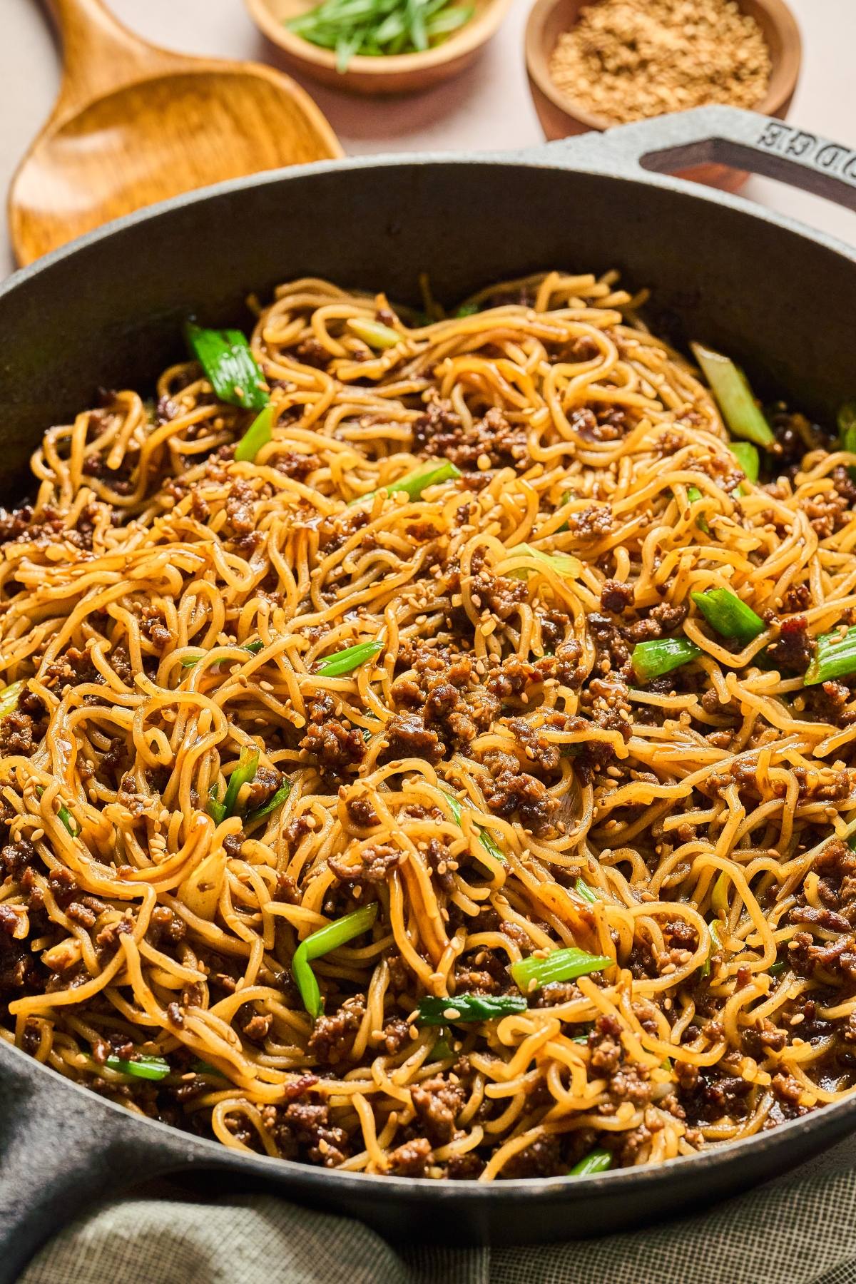 A skillet filled with stir-fried noodles, ground meat, green onions, and sesame seeds.