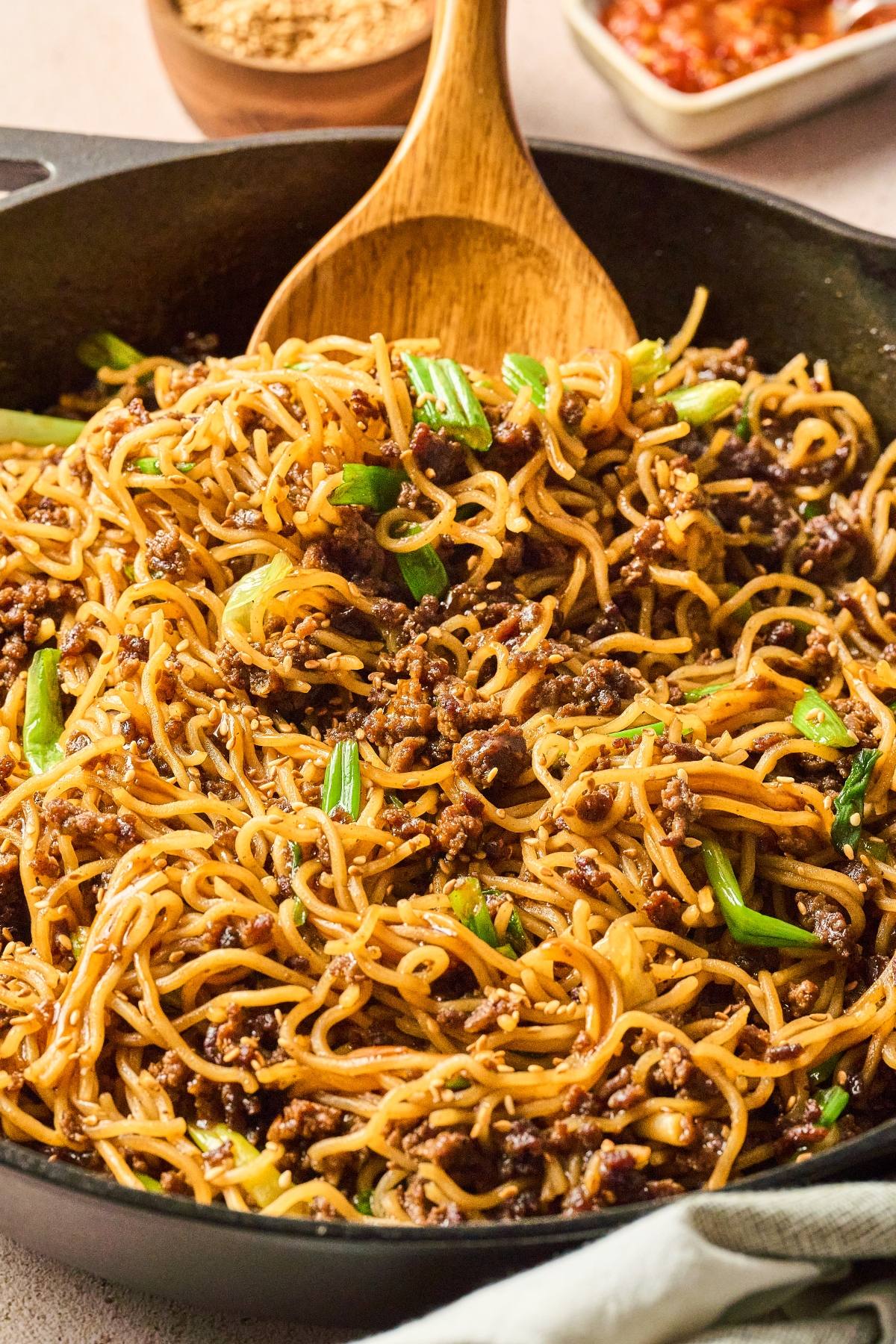 Stir-fried noodles with ground beef and green onions in a skillet, mixed with a wooden spoon.