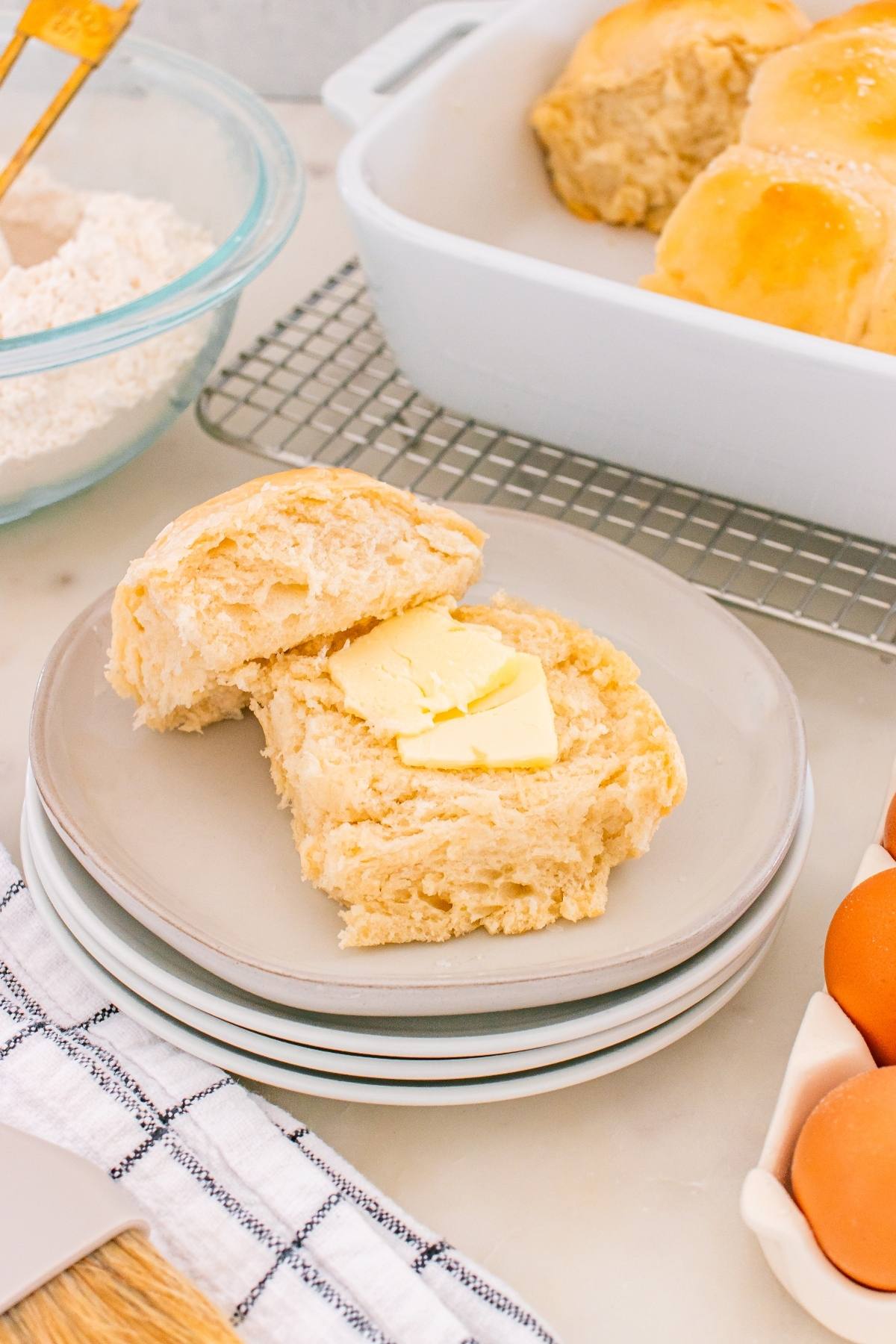 A biscuit split open with slices of butter on top, on a plate next to a dish of more biscuits.