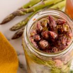 Open jar of Pickled Asparagus with fresh dill, beside whole asparagus spears and a yellow cloth for a vibrant, tangy display.