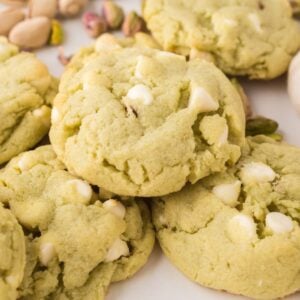 Pistachio Pudding Cookies with white chocolate chips, surrounded by pistachios on a white surface.