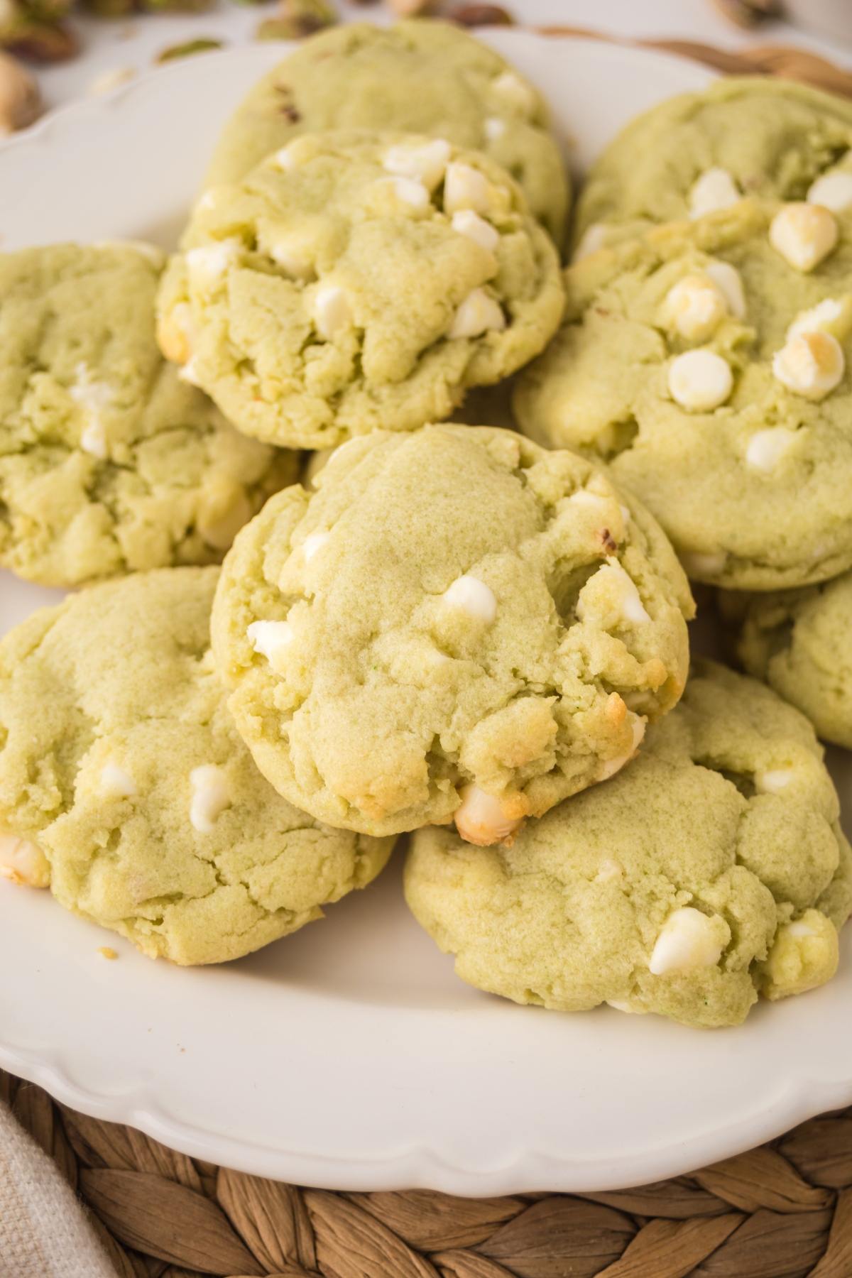 A plate of green cookies with white chocolate chips on a woven placemat.