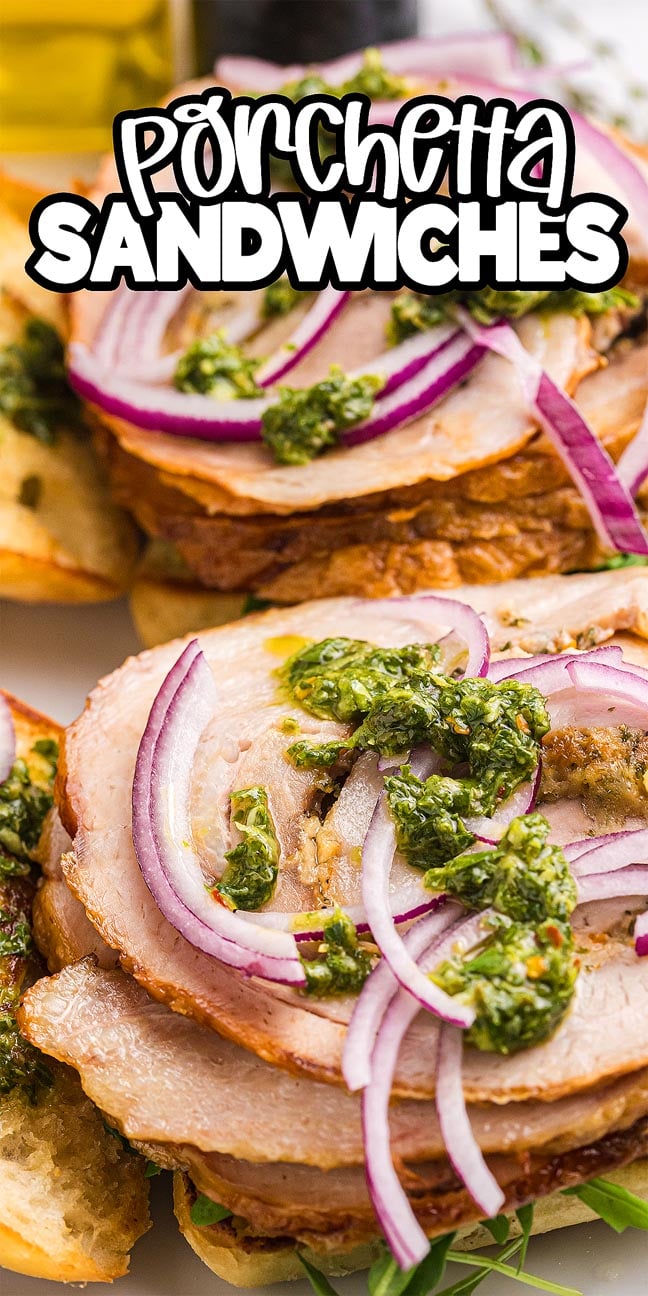 Close-up of a Porchetta Sandwich topped with red onion and green pesto on toasted bread.