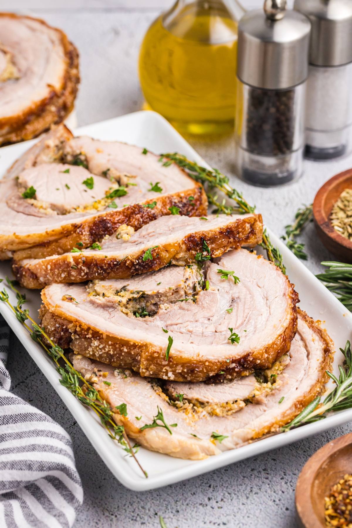 Sliced roasted pork with crispy skin on a white platter, garnished with herbs.