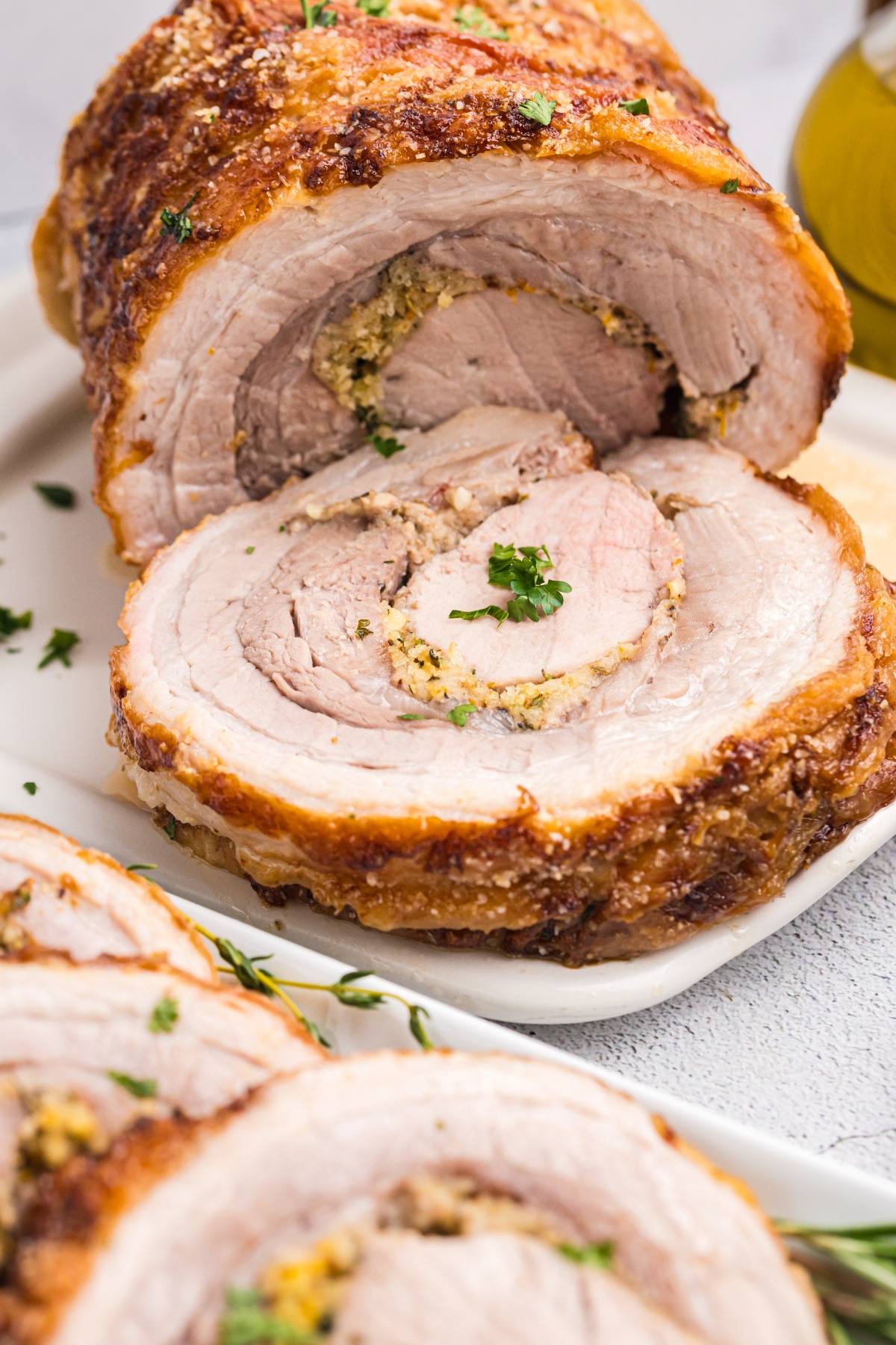 Sliced rolled roast pork with a golden crust and herb filling, garnished with chopped parsley on a white plate.