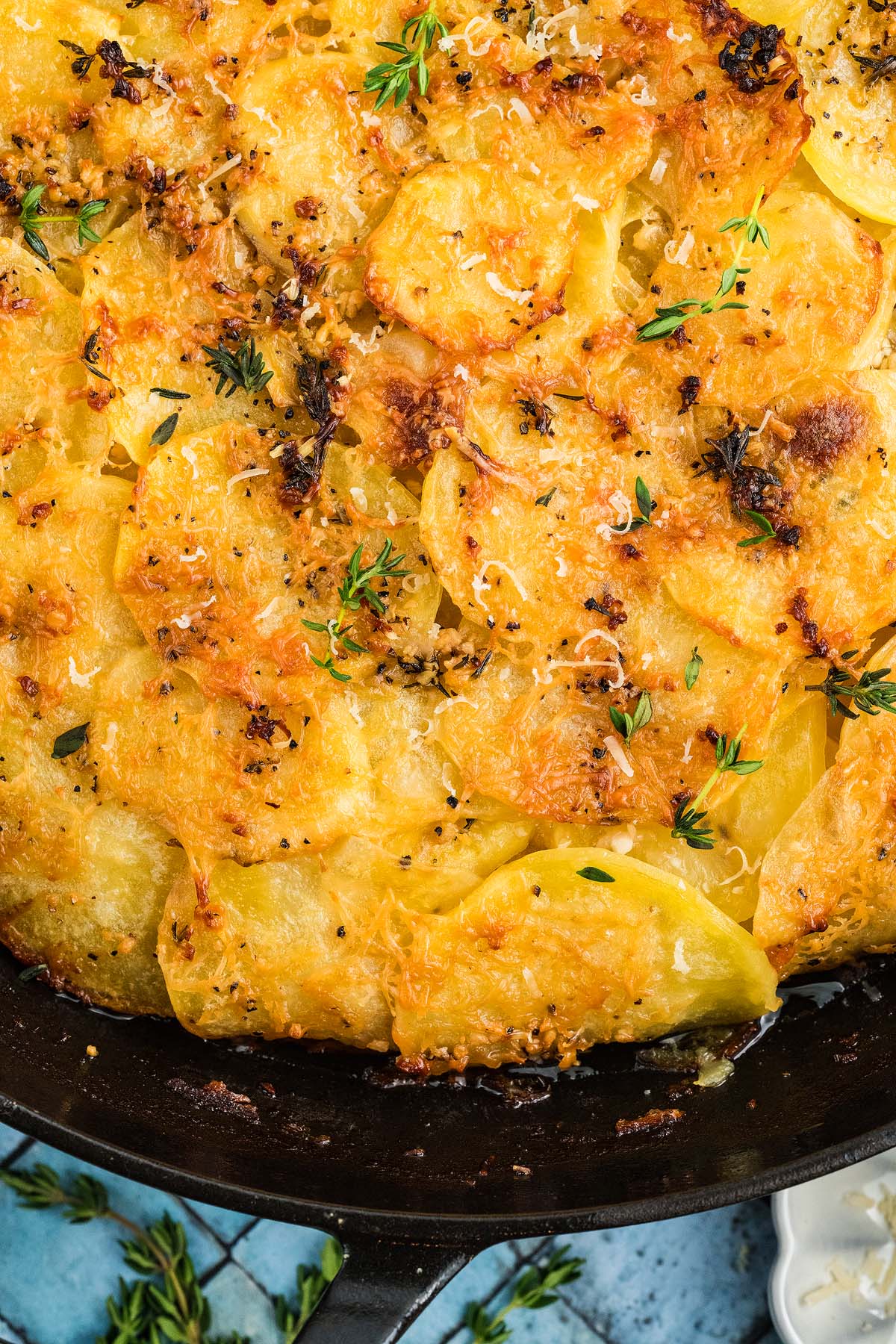 Golden, cheesy potato galette potatoes baked in a skillet, garnished with fresh thyme and crispy edges.