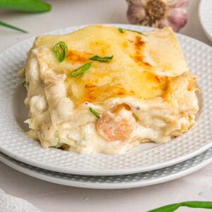 A slice of creamy seafood lasagna, garnished with green onions, is served on a white plate.