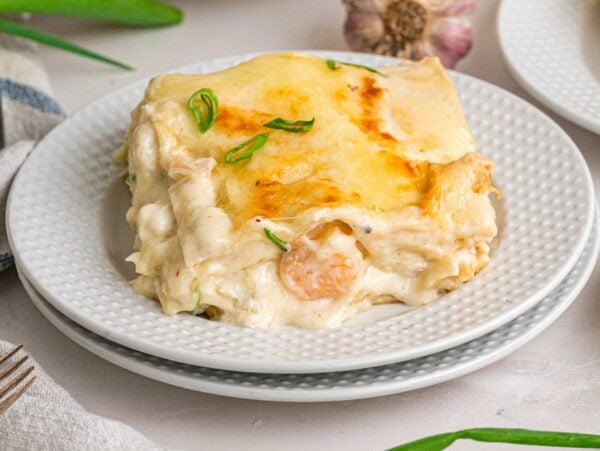 A slice of creamy seafood lasagna, garnished with green onions, is served on a white plate.