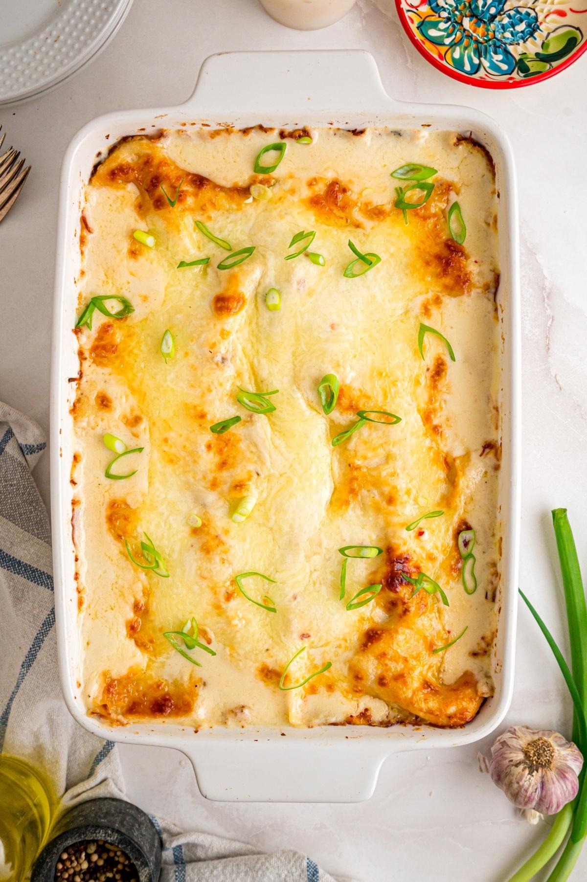 Baked creamy lasagna in a white dish, topped with melted cheese and chopped green onions.