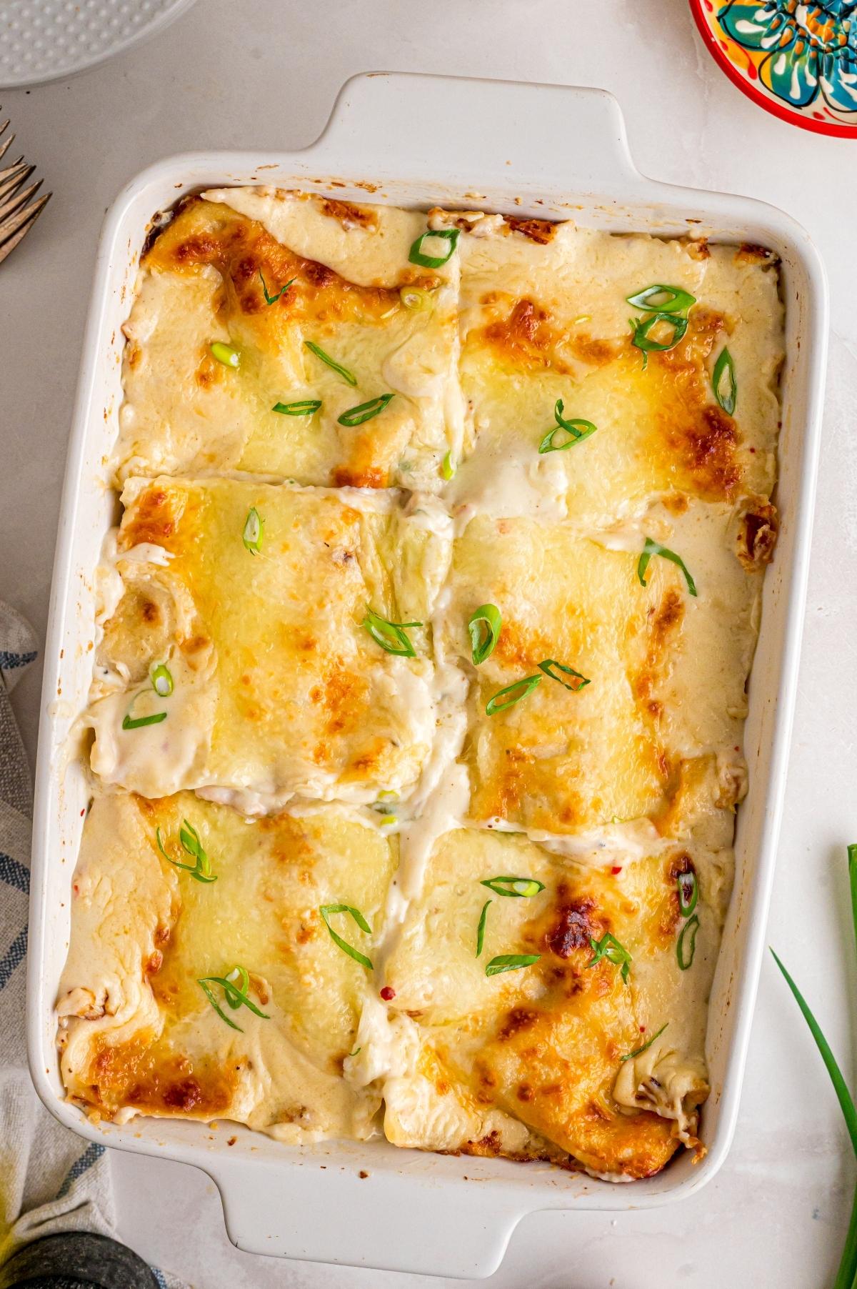 A baked cheesy lasagna in a white dish, topped with melted cheese and chopped green onions.